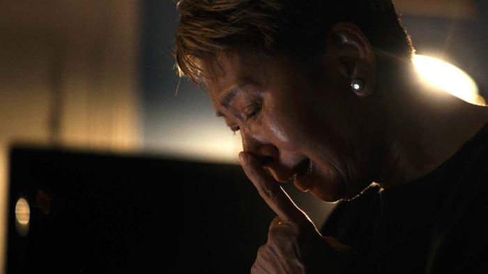 The Stringer: The Man Who Took the Photo movie: Vietnamese woman with short hair center holds hands to face while sitting in dark room