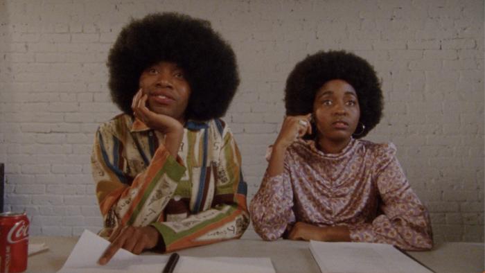 The Sweet East Movie: A Black man and woman sit at a table looking forward with interest