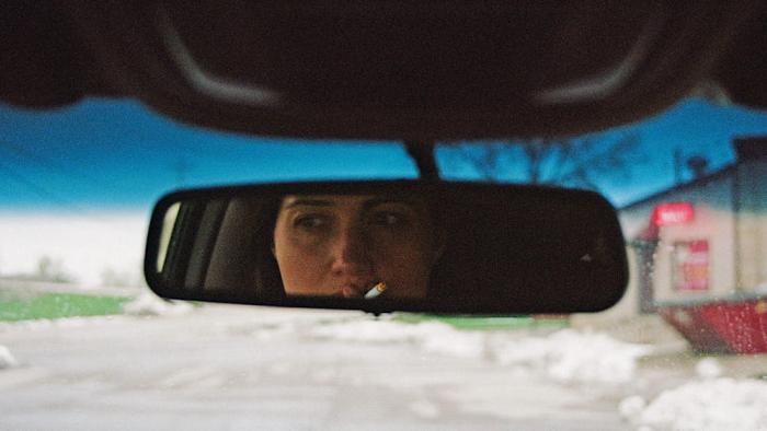 The Unknown Country movie: Lily Gladstone smokes a cigarette as she looks into her rearview mirror