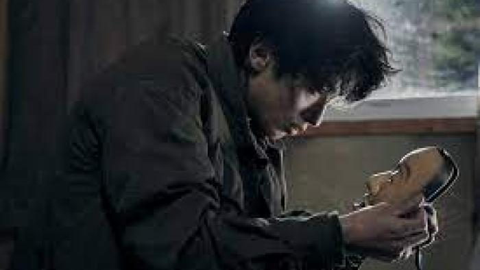 The Village (2023): A Japanese man center hunches over looking at a Japanese Noh mask in his hands