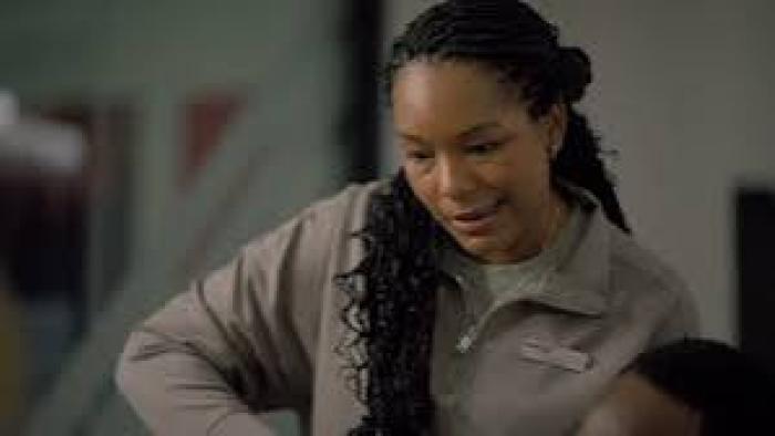 The Body in the Locker:  Black Woman with braided hair in a gray jacket, looking down with a gentle expression.