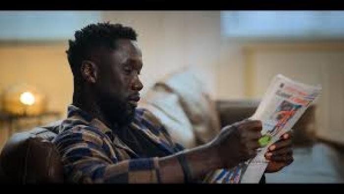 The Bus: A French Football Mutiny Movie: Black Man reading a newspaper on a cozy sofa indoors.