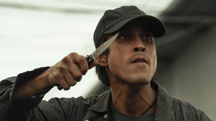 The Debt Collector Movie: Man in a cap holding a knife near his face, intense expression.