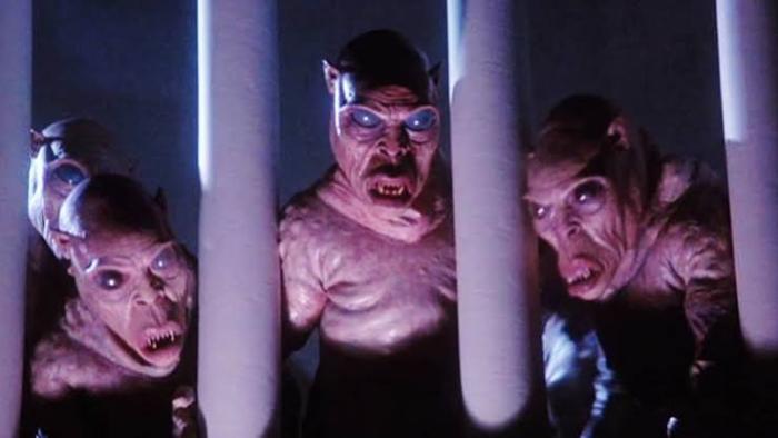 The Gate: Alien figures with glowing eyes look out from darkness behind bars.