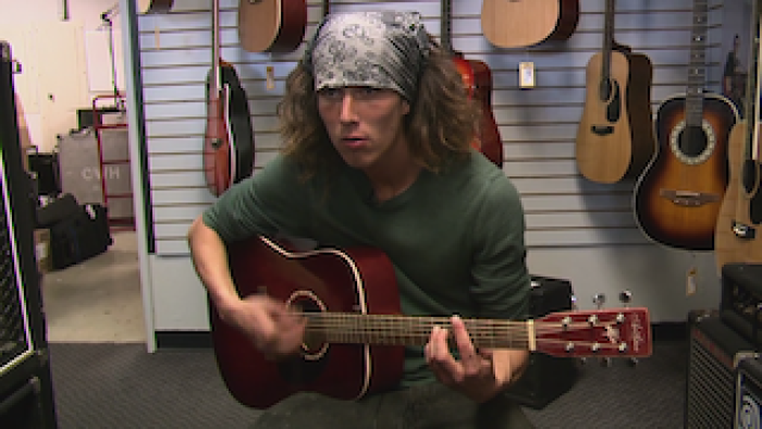 Caleb "Kai" McGillvary plays a guitar in a music store. 