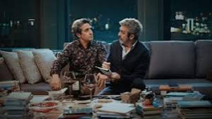 Therapy Done Right Movie: Two men sit on a couch, talking in a dimly lit room with books and snacks on the table.