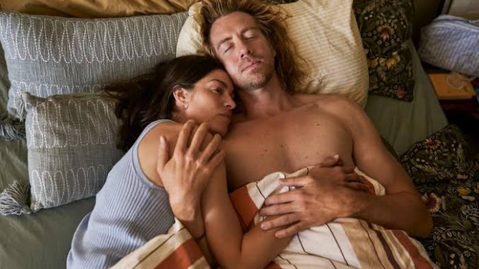 The Secret Woman:  Couple lying in bed, woman resting her head on man's chest, both appear relaxed.