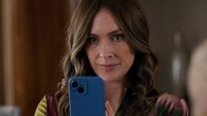 The Seemingly Perfect Family: Woman with long hair holding a blue smartphone, focused expression.