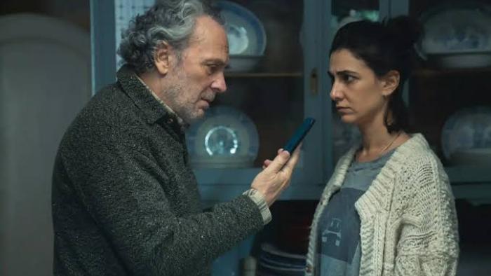 The Truthers Movie: Man showing phone to woman in a dimly lit kitchen.