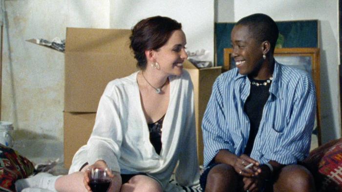 The Watermelon Woman: Two women sitting on a bed. One on the right wears a blue shirt. One on the left wears a white shirt. 