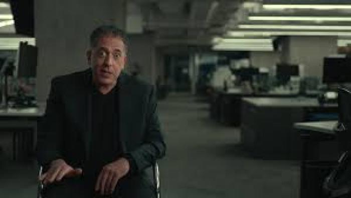The Widower: Man in a dark suit sitting in a dimly lit office setting.