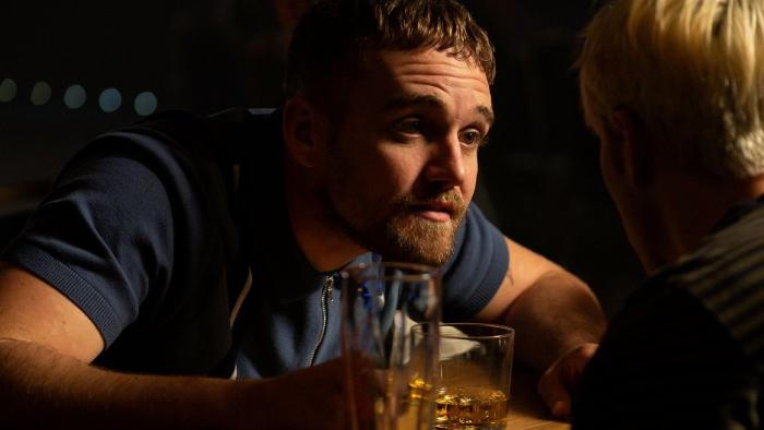 Three Day Millionaire: A young White man in a bar leans forward to talk intently to a friend
