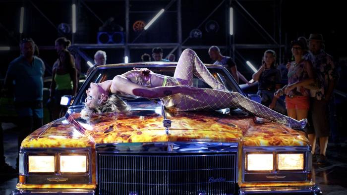 Titane: Woman dressed in underwear laying across bonnet of car