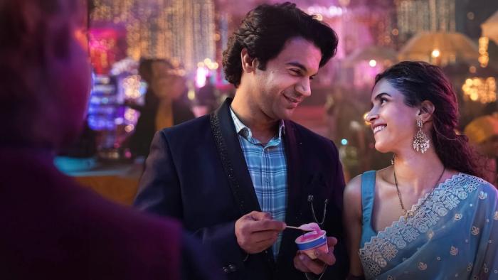 Toaster: Smiling Indian husband and wife in festive attire, sharing a moment with colorful lights in the background