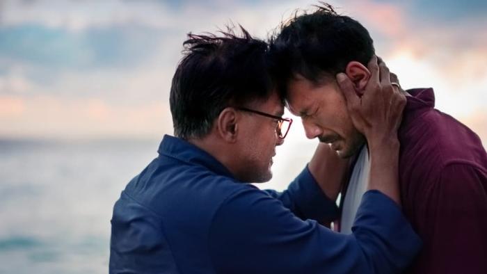 Today We'll Talk About That Day movie: Indonesian man in blue shirt center puts forehead to forehead of Indonesian man in red shirt on right