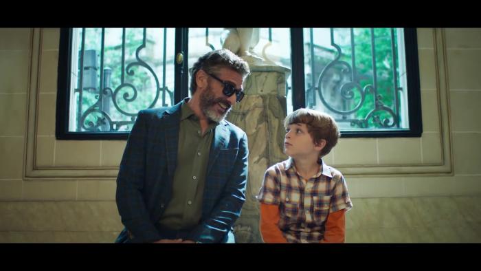 A man and boy sitting in front a window smile and talk.