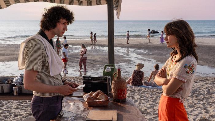 Tony movie: Dominic Sessa is a young Anthony Bourdain serving a clambake on the beach; Emilia Jones talks to him with her arms crossed