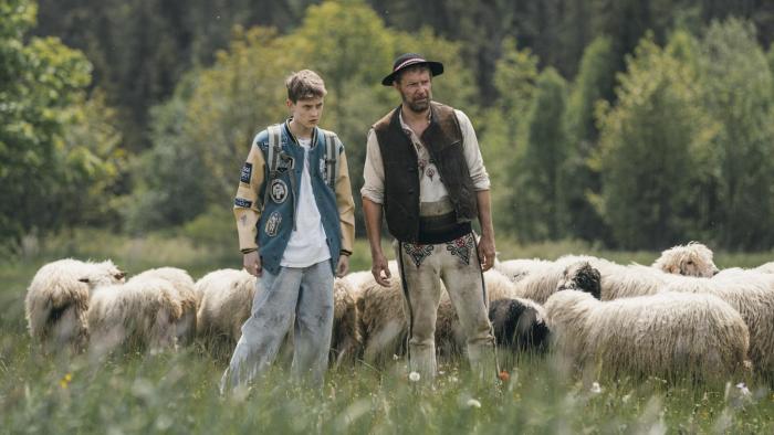 Too Old for Fairy Tales 2: A teen boy and a man stand with a flock of sheep