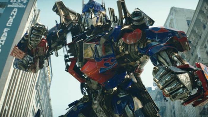Transformers Movie: Optimus Prime mecha stands in a fighting stance in front of buildings