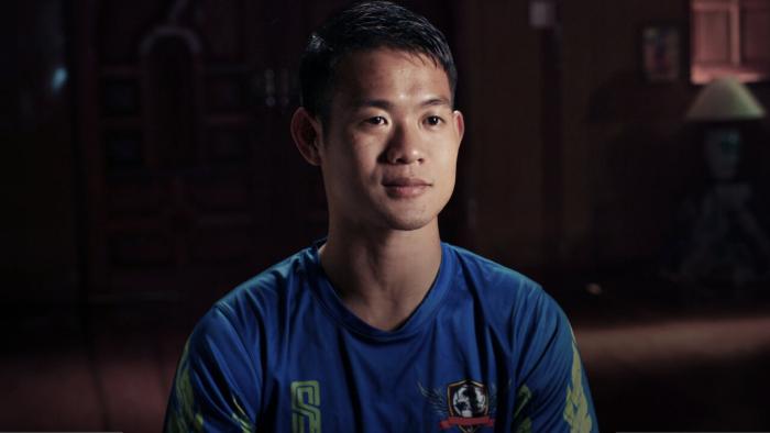 The Trapped 13 - How We Survived the Thai Cave: Thai man in his 20s "Coach Eik" wears a blue sports top during his interview.