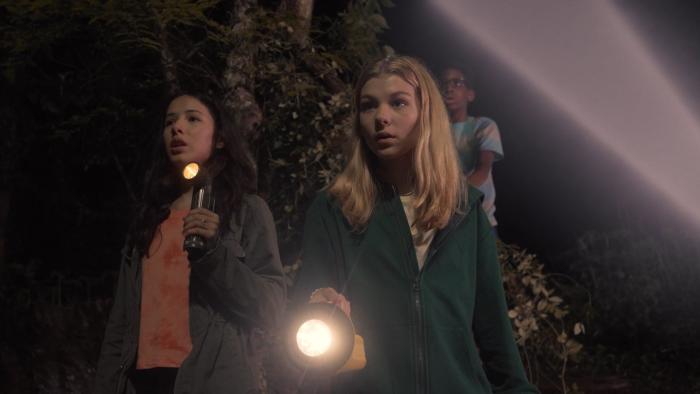 Treasure Trackers movie: Three kids walk in the dark while holding a flashlight