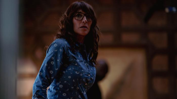 Trust movie: Katey Sagal, wearing glasses and a denim shirt with a flower print, looks at something apprehensively