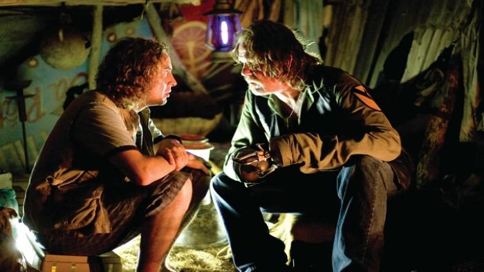 Tropic Thunder Movie: Two White men hunch in a dark tent looking bedraggled