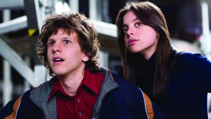 A close-up of Dyllan Christopher and Gia Mantegna: he is wearing a colored red shirt with a jacket, and she is wearing a black turtleneck.