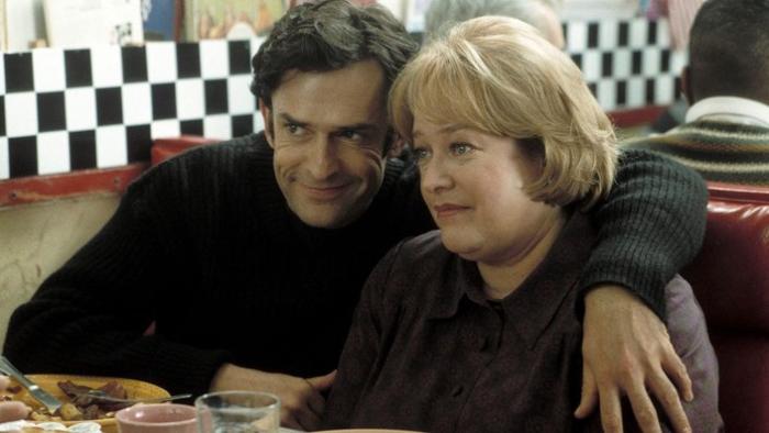 Rupert Everett puts his arm around Kathy Bates in a diner