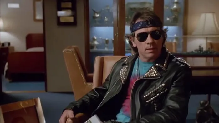 Under Siege: Man in sunglasses and leather jacket sitting indoors, looking to the side