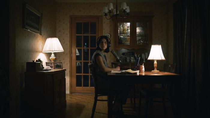 Undertone Movie: Seated at a kitchen table with her headphones and mic, Evy (Nina Kiri) looks as if she's heard something