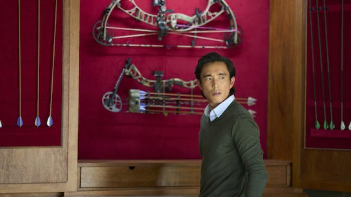 Untitled Home Invasion Romance: Justin H. Min in front of a weapons cache.