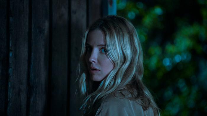 Vanished into the Night movie: White Italian woman with blond hair center turns around in front of wooden door at night
