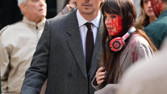 Verity movie: A man in a suit and woman with headphones, both covered in blood, in a street scene