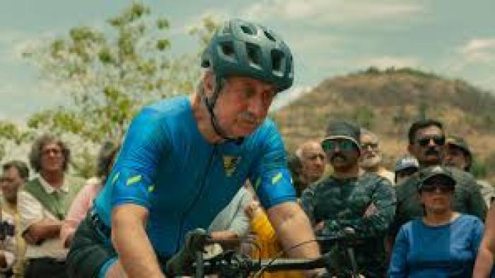 Vijay 69 movie: Older Indian man in blue tracksuit and helmet rides bicycle in a race while a crowd looks on