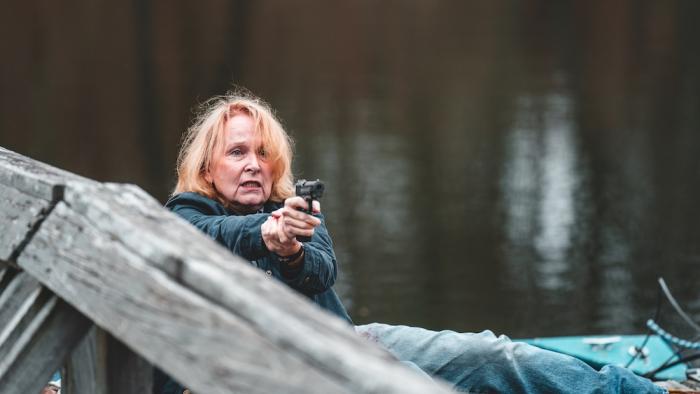 Violent Ends Movie: Deputy Sheriff Darlene Woodley (Kate Burton) hoists her gun, lying on one side on a wooden dock