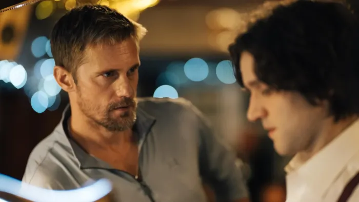 Pillion: A White leaning over a bar next to a younger White man