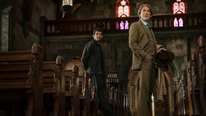Wake Up Dead Man movie: Benoit Blanc (Daniel Craig) stands inside a cathedral while priest Jud (Josh O'Connor) sits on the edge of a pew