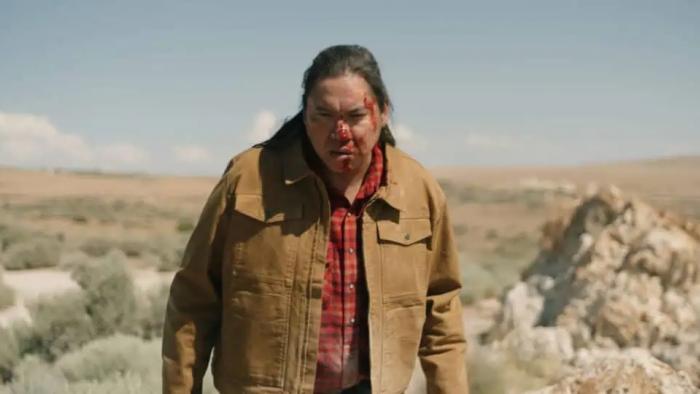 Wardriver movie: William Belleau stands in the desert with blood on his face, peering down at something