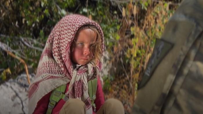 Warhorse One: A young girl sits on rock wearing headscarf.