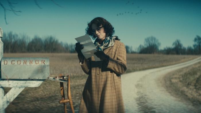 Wildcat Movie: Flannery O'Connor (Maya Hawke) stands by a mailbox near a country road, reading a letter