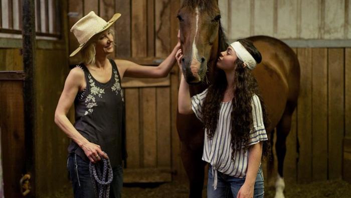 Wildfire: The Legend of the Cherokee Ghost Horse movie: Anne Heche and a teen girl with a bandaged head pet a horse in a stable
