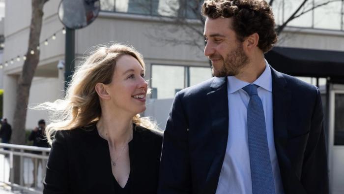 You Can See Everything movie: Theranos founder Elizabeth Holmes and partner Billy Evans smile at each other while walking down a street
