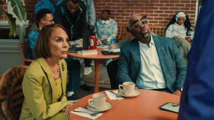 A Different World TV screenshot 1: Jasmine Guy and Kadeem Hardison sit at a dining table. Guy wears a green suit, Hardison wears flip-up sunglasses.