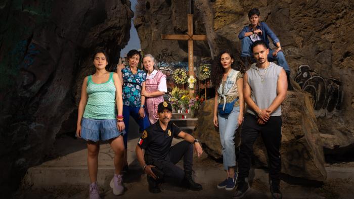We Were Kings TV show screenshot 1: An ensemble of Mexican men and women stand in front of a memorial with a wooden cross with the name "Santos" on it