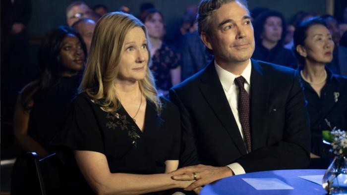 American Classic TV show screenshot 3: Laura Linney and Jon Tenney sit in an audience. Linney wears a black dress, Tenney wears a black suit jacket.