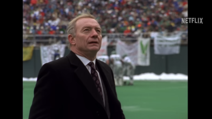 Archival footage photo of Jerry Jones, clad in a suit, standing on a football field in a packed stadium