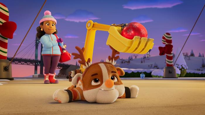 A PAW Patrol Christmas TV show screenshot 2: Rubble lays on the ground with paws spread out, looking at the Christmas ornament his gripper caught.