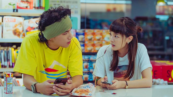 At the Moment TV show screenshot 1: Two young people inside a convenience store share a set of wired earbuds
