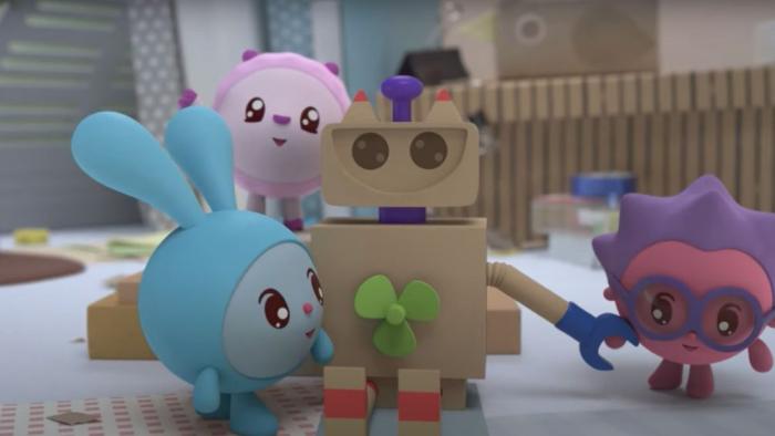 Baby Riki: Two characters play with a cardboard robot toy in a bright nursery room with wooden fence background.